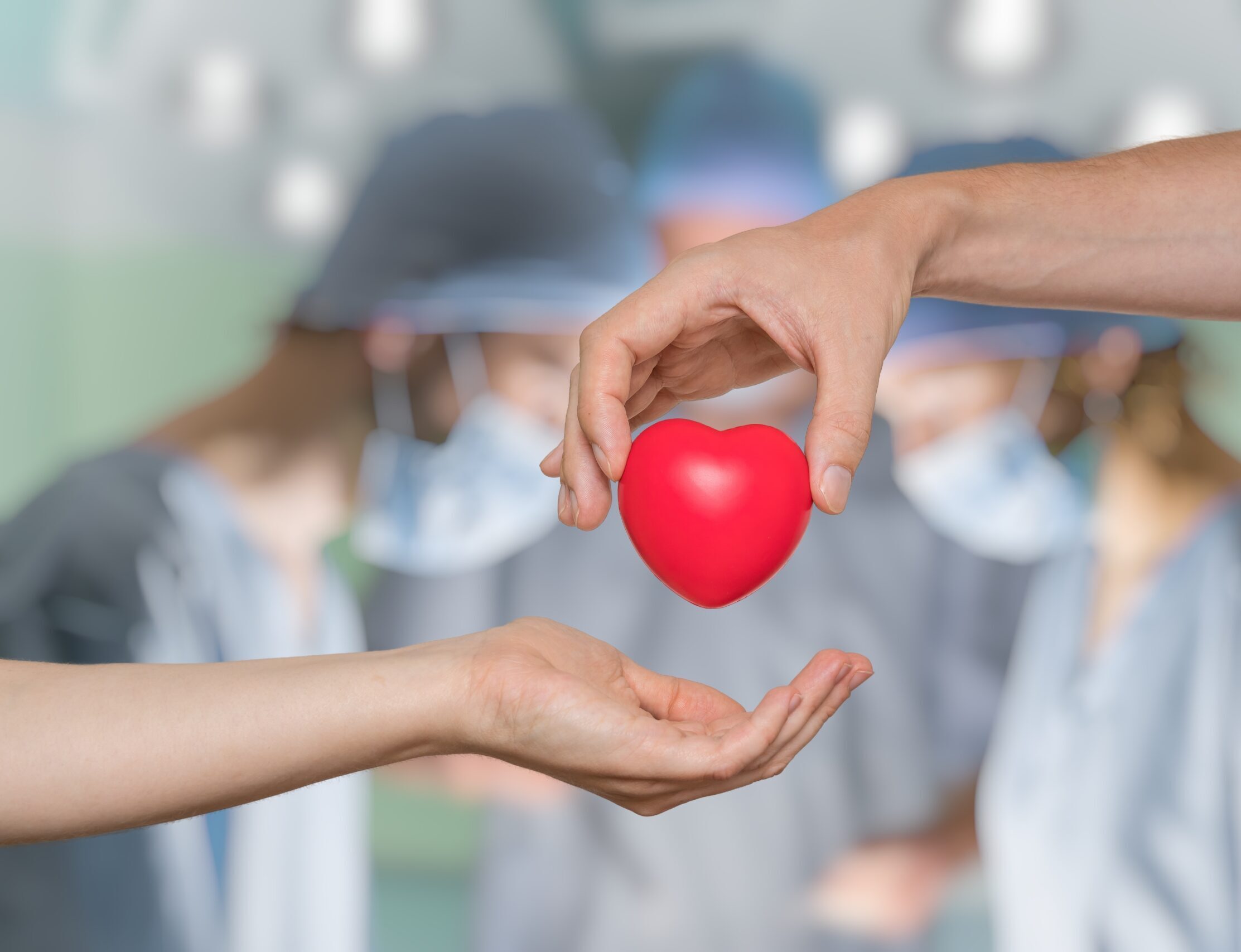 Hands holding a model of a heart, with three masked physicians in the background