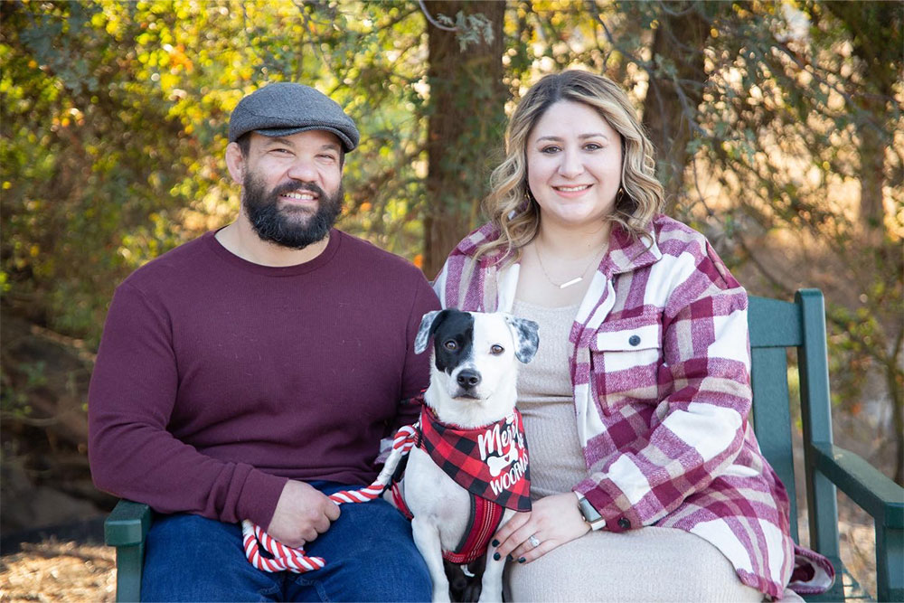Man and a woman sit with a dog in between them.